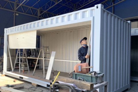 コンテナの側面にシャッターを取り付けている作業の様子