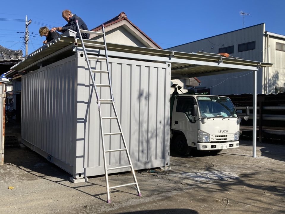 コンテナと柱の上に屋根材を取り付けている作業の様子