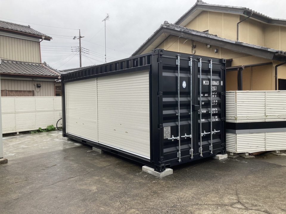 住宅の駐車場に側面シャッター付きの黒いコンテナを設置した様子