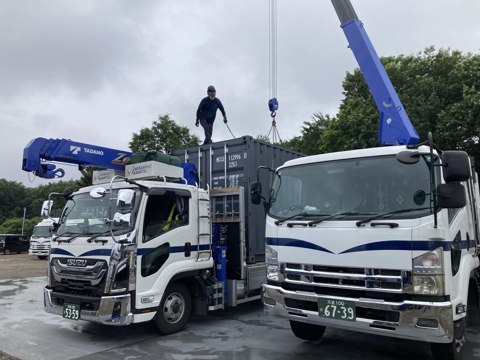 クレーン付きトラック2台でコンテナを搬送・設置している様子